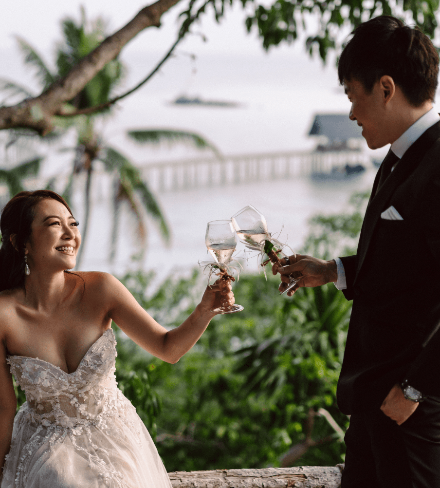 wedding couple cheers with champagne glasses at the Lookout, jetty in background. WEDDINGS & VOW RENEWAL CEREMONIES at Bawah Reserve, Indonesia.
